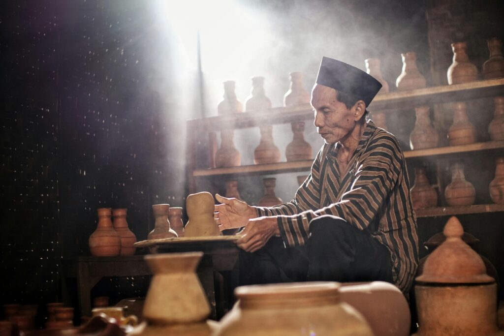 A potter skillfully crafts pottery in a traditional Indonesian workshop with natural lighting.