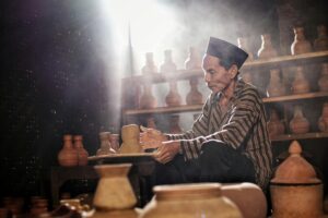 A potter skillfully crafts pottery in a traditional Indonesian workshop with natural lighting.