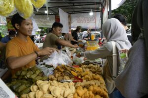A busy street food market with vendors selling traditional snacks to customers.