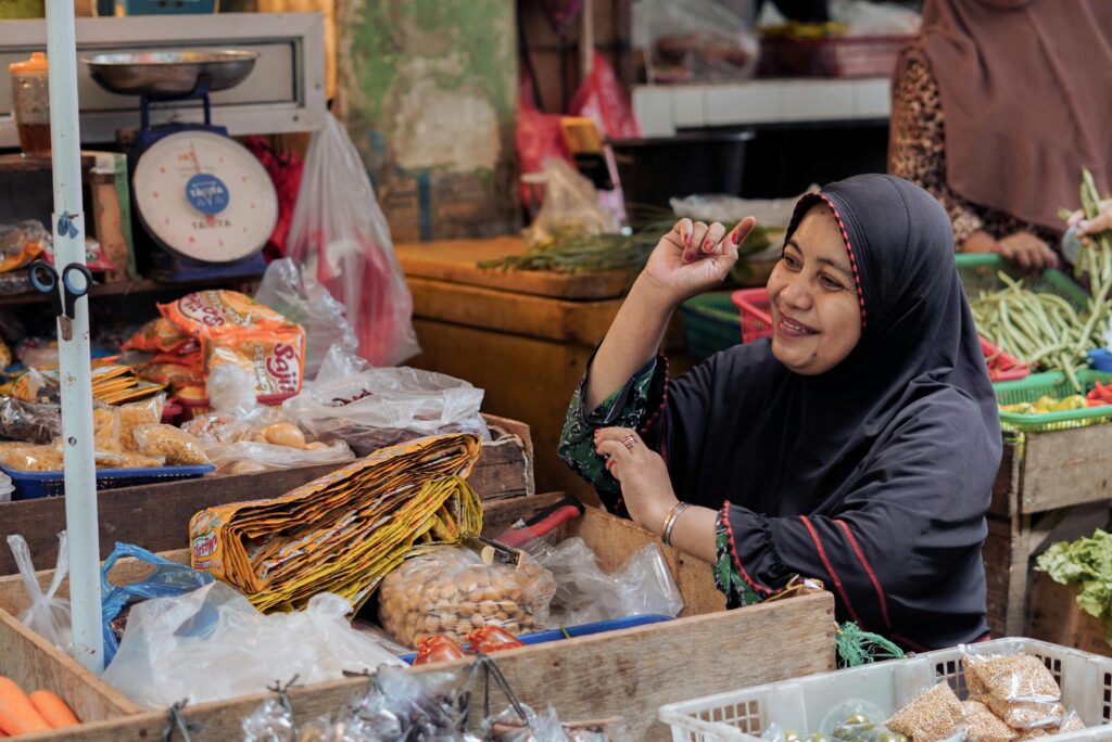 A smiling vendor in a hijab at a bustling market in Pontianak, Indonesia.
