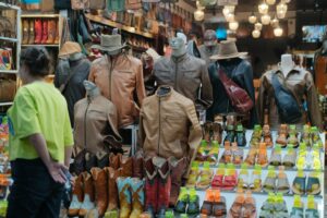 Mannequins displaying diverse leather goods at a bustling market stand.