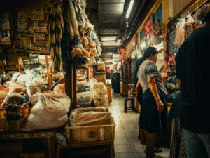 A busy indoor market scene featuring various goods and shoppers exploring the aisles.