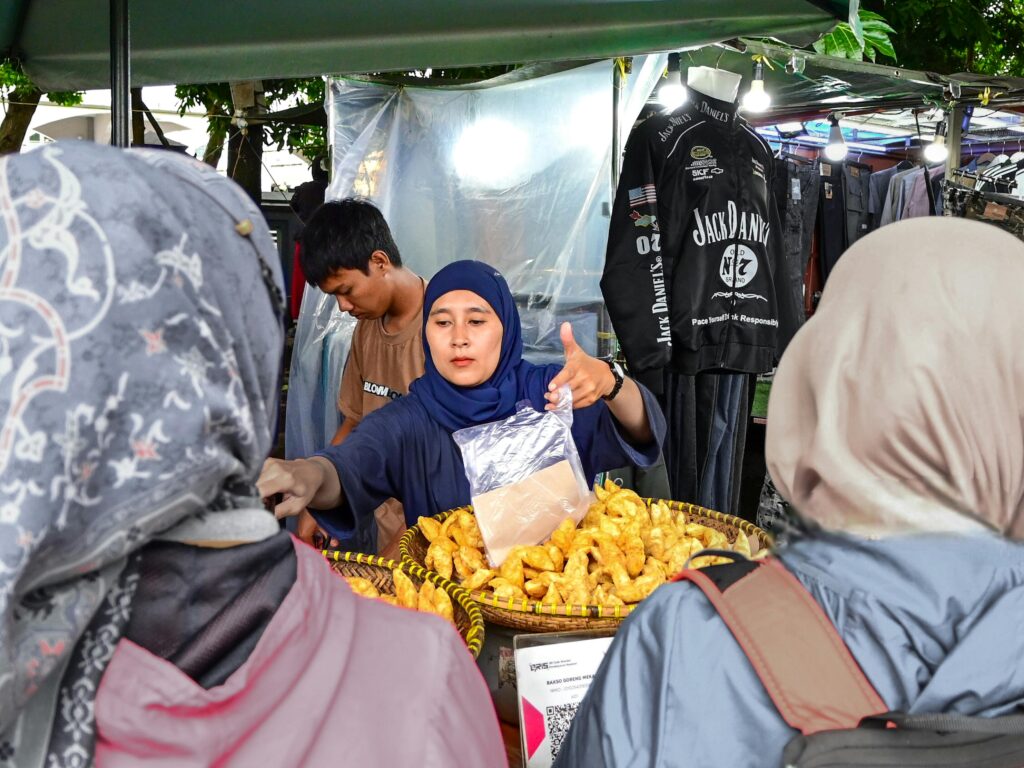 A woman selling pastries at an outdoor market booth during the day.