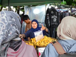 A woman selling pastries at an outdoor market booth during the day.
