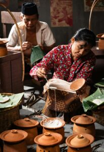 Indonesian woman and man preparing traditional meal with clay pots, showcasing cultural heritage.