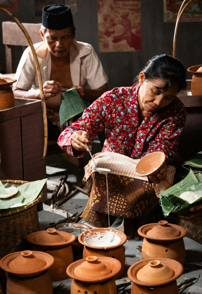 Indonesian woman and man preparing traditional meal with clay pots, showcasing cultural heritage.