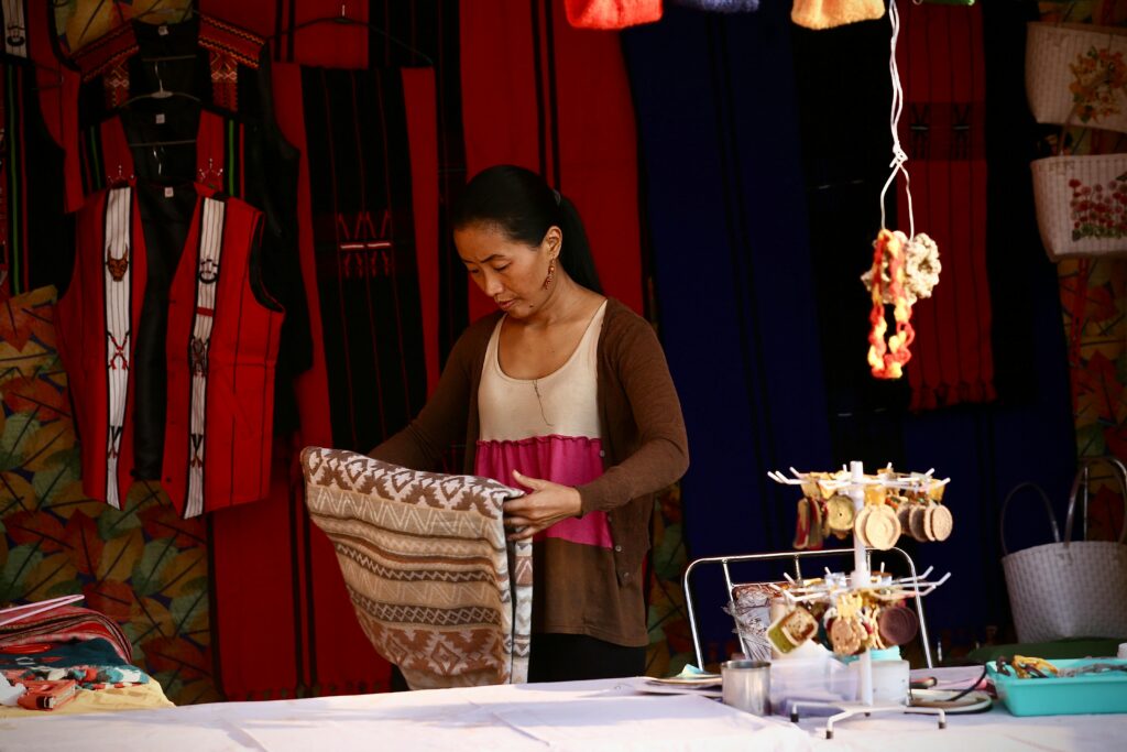 A woman organizing traditional handwoven textiles at a colorful outdoor market stall.