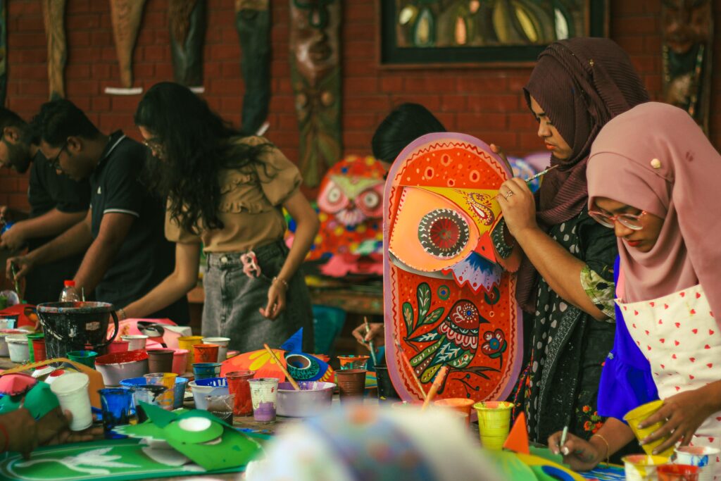 A vibrant group art workshop at the University of Dhaka, with participants painting colorful masks.
