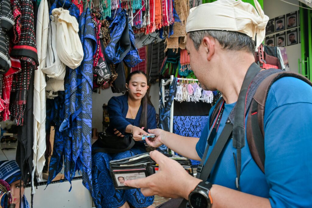 A man buying textiles at an outdoor market stall from a female vendor.